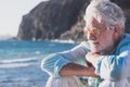 Portrait of handsome senior man, white haired, sitting on the beach looking at horizon over water