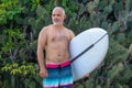 Portrait of handsome shirtless man surfer, holding white surf board and green cactus on background