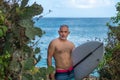 Portrait of handsome shirtless man surfer, holding white surf board and green cactus on background