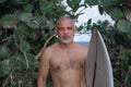 Portrait of handsome shirtless man surfer, holding white surf board and green cactus on background