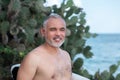 Portrait of handsome shirtless man surfer, holding white surf board and green cactus on background