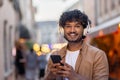 Portrait of a handsome smiling Indian man looking at the camera. Standing on a city street in white headphones and Royalty Free Stock Photo