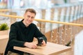 Portrait of handsome smiling young man sitting at table in cozy coffee shop enjoying time alone with coffee cup and Royalty Free Stock Photo