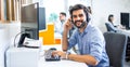 Portrait of handsome smiling young man working in a call center with his colleagues in the background. Royalty Free Stock Photo