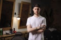 Portrait of handsome stylish young barber with tattoos stands with crossed arms at barber shop and confidently looking Royalty Free Stock Photo