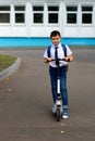 Portrait of a handsome stylish and young schoolboy in a white shirt, blue tie and a backpack with a scooter Royalty Free Stock Photo