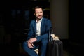 Portrait of a handsome successful man, confident businessman, smiling investor sitting in a chair in a hotel lobby with a luggage Royalty Free Stock Photo