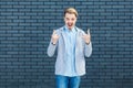 Portrait of handsome surprised young blonde man in casual style standing with rock and roll horns gesture and looking at camera