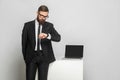 Portrait of handsome thoughful bearded young businessman in corporated format wear in black suit are standing and checking time on