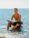 Portrait of handsome topless male model on the sea beach. Sporty man sit on the stone with diving fins and mask