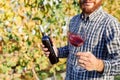Portrait of handsome wine maker holding in his hand bottle and a glass of red wine and tasting it, checking wine quality while Royalty Free Stock Photo