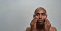 Portrait of handsome young african american man looking at camera, applying cream on his face, posing  over gray Royalty Free Stock Photo