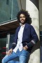 Portrait of handsome young Afro American man in casual clothes, looking camera and smiling while leaning on a column, standing Royalty Free Stock Photo