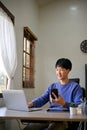 Portrait of handsome young Asian male office worker sits at his desk, using laptop Royalty Free Stock Photo