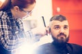 Portrait of handsome young bearded caucasian man getting trendy haircut in modern barber shop. Royalty Free Stock Photo