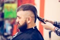 Portrait of handsome young bearded caucasian man getting trendy haircut in modern barber shop. Royalty Free Stock Photo