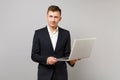 Portrait of handsome young business man in classic black suit, shirt hold laptop pc computer isolated on grey wall Royalty Free Stock Photo