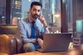 Portrait of handsome young business man with laptop talking on mobile phone in modern office. Royalty Free Stock Photo