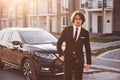 Portrait of handsome young businessman in black suit and tie outdoors near modern car in the city Royalty Free Stock Photo