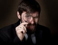 Portrait of handsome young businessman looking through magnifying glass on a brown background Royalty Free Stock Photo