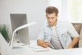 Portrait of handsome young businessman sitting at office table with personal computer and writing on mobile phone Royalty Free Stock Photo