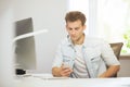 Portrait of handsome young businessman sitting at office table with personal computer and writing on mobile phone Royalty Free Stock Photo