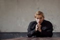 Portrait of handsome young catholic priest praying to God. Dark style, concept doubt