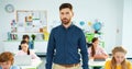 Portrait of handsome young Caucasian male tutor standing in classroom looking at camera and smiling. Children using Royalty Free Stock Photo