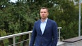 Portrait of handsome young classy man in suit walking outdoors in city. Caucasian confident successful businessman walks