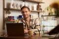 Portrait of handsome young digital nomad, man working in cafe on laptop, looking happy and pleased with his online Royalty Free Stock Photo