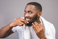 Portrait of handsome young african american black man combing his beard in bathroom. Isolated over grey background