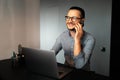 Portrait of handsome young happy man, working home at laptop, talking on smartphone with clients, looking away. Wearing eyeglasses Royalty Free Stock Photo