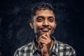 Portrait of a handsome young Indian guy wearing a checkered shirt holding hand on chin and looking at a camera with a Royalty Free Stock Photo
