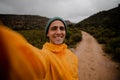 Portrait handsome young male hiker smiling at camera after steep hike on gravel mountain trail in cold cloudy weather Royalty Free Stock Photo
