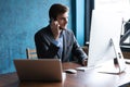 Portrait of handsome young male sitting at office desk with laptop computer and talking on mobile phone. Communication Royalty Free Stock Photo