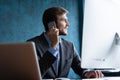 Portrait of handsome young male sitting at office desk with laptop computer and talking on mobile phone. Communication Royalty Free Stock Photo