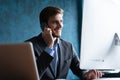 Portrait of handsome young male sitting at office desk with laptop computer and talking on mobile phone. Communication Royalty Free Stock Photo