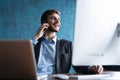 Portrait of handsome young male sitting at office desk with laptop computer and talking on mobile phone. Communication Royalty Free Stock Photo