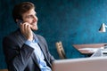 Portrait of handsome young male sitting at office desk with laptop computer and talking on mobile phone. Communication Royalty Free Stock Photo