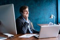 Portrait of handsome young male sitting at office desk with laptop computer and talking on mobile phone. Communication Royalty Free Stock Photo