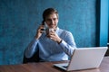 Portrait of handsome young male sitting at office desk with laptop computer and talking on mobile phone. Communication Royalty Free Stock Photo