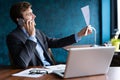 Portrait of handsome young male sitting at office desk with laptop computer and talking on mobile phone. Communication Royalty Free Stock Photo