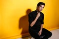 Portrait of a handsome young man in black clothing, seated on chair on yellow background. Horizontal view Royalty Free Stock Photo