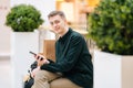 Portrait of handsome young man holding using mobile phone sitting on bench in shopping mall looking at camera Royalty Free Stock Photo