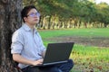 Portrait of a handsome young man with a laptop computer leaning on a tree and looking far away in nature background with copy spac Royalty Free Stock Photo