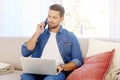 Young man using mobile phone and notebook while sitting on couch at home Royalty Free Stock Photo