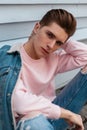 Portrait handsome young man model in trendy pink sweatshirt in fashion denim blue youth jacket near white wall outdoors. Urban guy Royalty Free Stock Photo