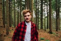 Portrait of a handsome young man in red standing in a coniferous forest and posing for the camera with a smile on his face. Royalty Free Stock Photo