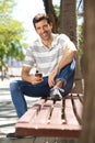 Handsome young man sitting outdoors on bench with mobile phone Royalty Free Stock Photo