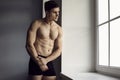 Portrait of handsome young man with sporty body posing in underwear standing by window. Royalty Free Stock Photo